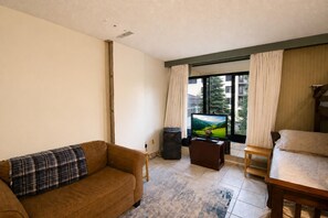 A living room with a sofa, a television, a small table, and a window with curtains. - SC 2207 | Mountain Summer Escape with Refreshing Pool Access (Snowshoe)