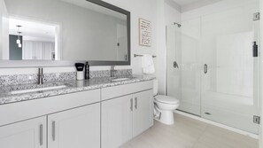 A modern bathroom with a granite countertop, a white toilet, a glass shower enclosure, and a large mirror. - Landing | Modern 1BD, Yoga Studio, Gym (Sarasota)