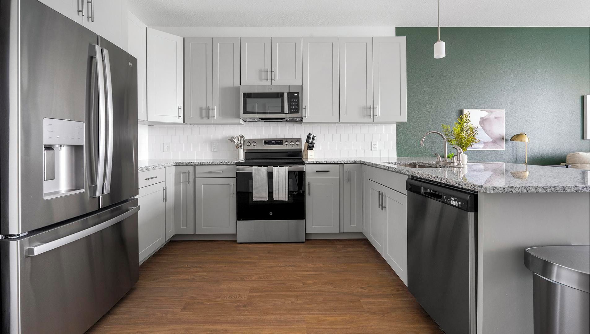 A modern kitchen with stainless steel appliances, white cabinetry, and a wooden floor.