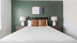 A neatly made bed with white linens, two brown pillows, and two bedside lamps on wooden nightstands. - Landing | Stunning 1BD, Gym, Yoga Studio (Sarasota)