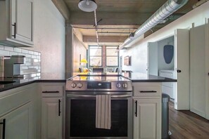A kitchen with white cabinets, a stainless steel stove, and a window providing natural light. - Landing | Incredible 1BD, Gym, Pool (Kansas City)