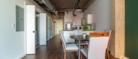 A modern kitchen with white cabinets and a central island, a dining area with a round table and chairs, and exposed ductwork on the ceiling.