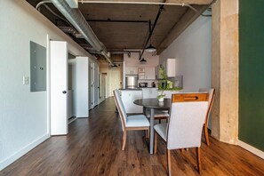 Eine moderne Küche mit weißen Schränken und einer zentralen Kochinsel, ein Essbereich mit rundem Tisch und Stühlen sowie freiliegende Lüftungsrohre an der Decke.