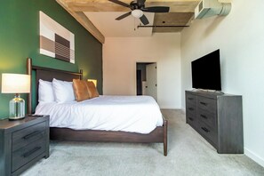 Ein Schlafzimmer mit Bett, Nachttisch, Lampe, Kommode, Fernseher, Deckenventilator und einer Tür zu einem anderen Raum.