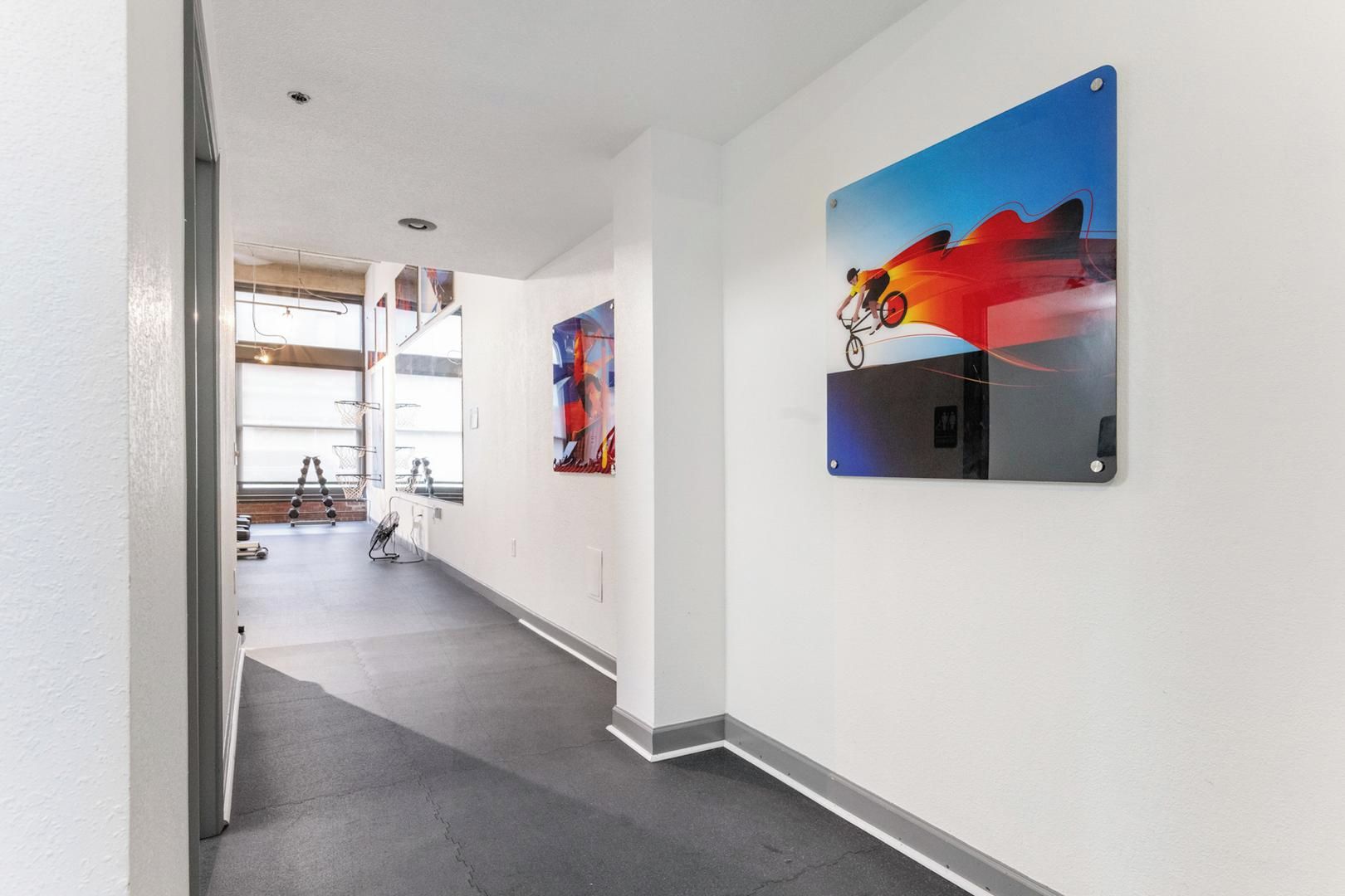 Un couloir avec un escalier menant à une salle de sport, une œuvre d’art accrochée au mur et un cadre de porte.