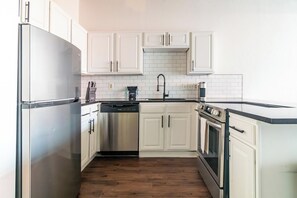 A modern kitchen with white cabinetry, stainless steel appliances, and a wooden floor. - Landing | Incredible 1BD, Gym, Pool (Kansas City)
