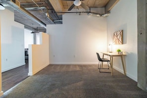 A modern office space with a carpeted floor, a desk with a chair, a ceiling fan, and ductwork. - Landing | Incredible 1BD, Gym, Pool (Kansas City)