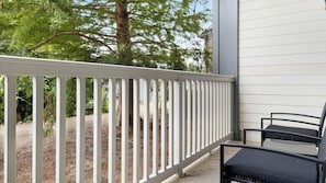 A balcony with a white railing, a black chair, and a tree in the background. - Landing | Amazing 1BD, Gym (Gainesville)