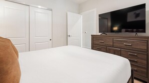 Quarto com cama, cômoda, televisão e três portas fechadas.
