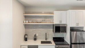 Eine moderne Küche mit weißen Schränken, einem Edelstahlkühlschrank, einem eingebauten Ofen und einer Kaffeemaschine.