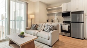 Eine moderne Küche mit einem Edelstahl-Kühlschrank, einem Einbauofen und einer Mikrowelle. Es gibt ein graues Sofa mit gemusterten Kissen und einen kleinen Holztisch mit einer Pflanze.