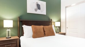Ein Hotelzimmer mit einem Bett, zwei Nachttischen, einer Kommode, einer Tür und einem an der Wand hängenden Kunstwerk.