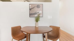 A round table with two brown chairs, a vase with green plants, and a framed abstract artwork on the wall. - Landing | Amazing 1BD in Kannapolis (Kannapolis)