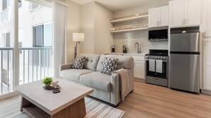 Ein modernes Apartment mit einer Couch, einem Esstisch, einer Küche mit Edelstahlgeräten und Blick durch große Fenster.
