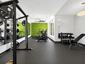 A modern gym with a weightlifting area, cardio machines, and a green wall.