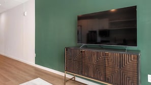 A flat-screen TV mounted on a wall above a wooden cabinet with a geometric pattern. - Landing | Beautiful 1BD in Kannapolis (Kannapolis)