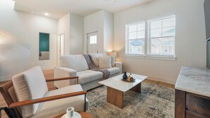 A modern living room with a sofa, coffee table, and a dining area. - Landing | Stunning 2BD, Gym (Palmetto)