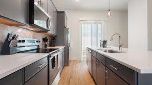 A modern kitchen with stainless steel appliances, a built-in oven, and a large island with a sink. - Landing | Stunning 2BD, Gym (Palmetto)