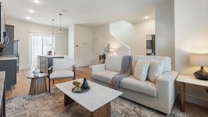 A modern living room with a sofa, coffee table, and a dining area with a chair and table. - Landing | Stunning 2BD, Gym (Palmetto)