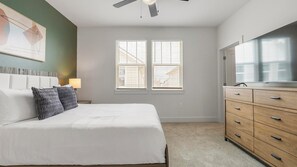 Ein Schlafzimmer mit Bett, Kommode, Deckenventilator und einem Fenster mit Jalousien.
