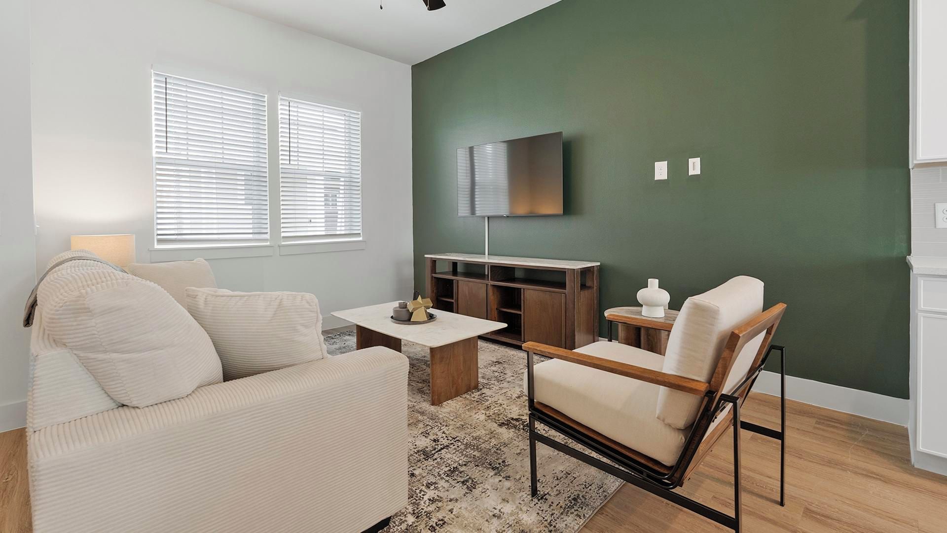 Ein Wohnzimmer mit einer Couch, einem Couchtisch, einem an der Wand montierten Fernseher und einem Holzkasten.