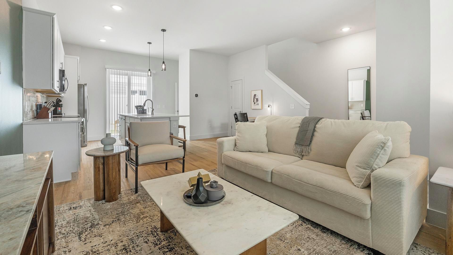 A modern living room with a sofa, coffee table, and a dining area with a kitchen in the background.