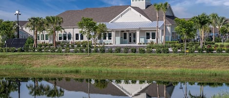 A waterfront property with a reflective pond, a white building with a tower, and palm trees.