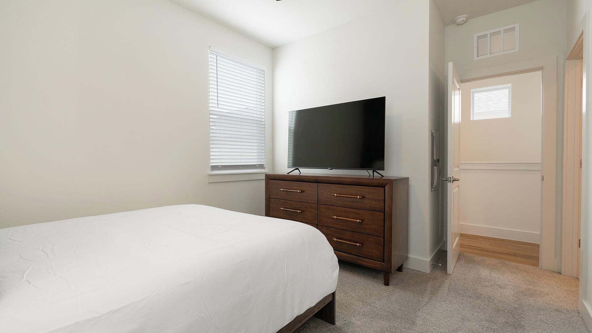 A bedroom with a bed, a dresser, a television, and a door.