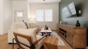 Ein Wohnzimmer mit einer Couch, einem Couchtisch, einem an der Wand befestigten Fernseher und einem Holzschrank.