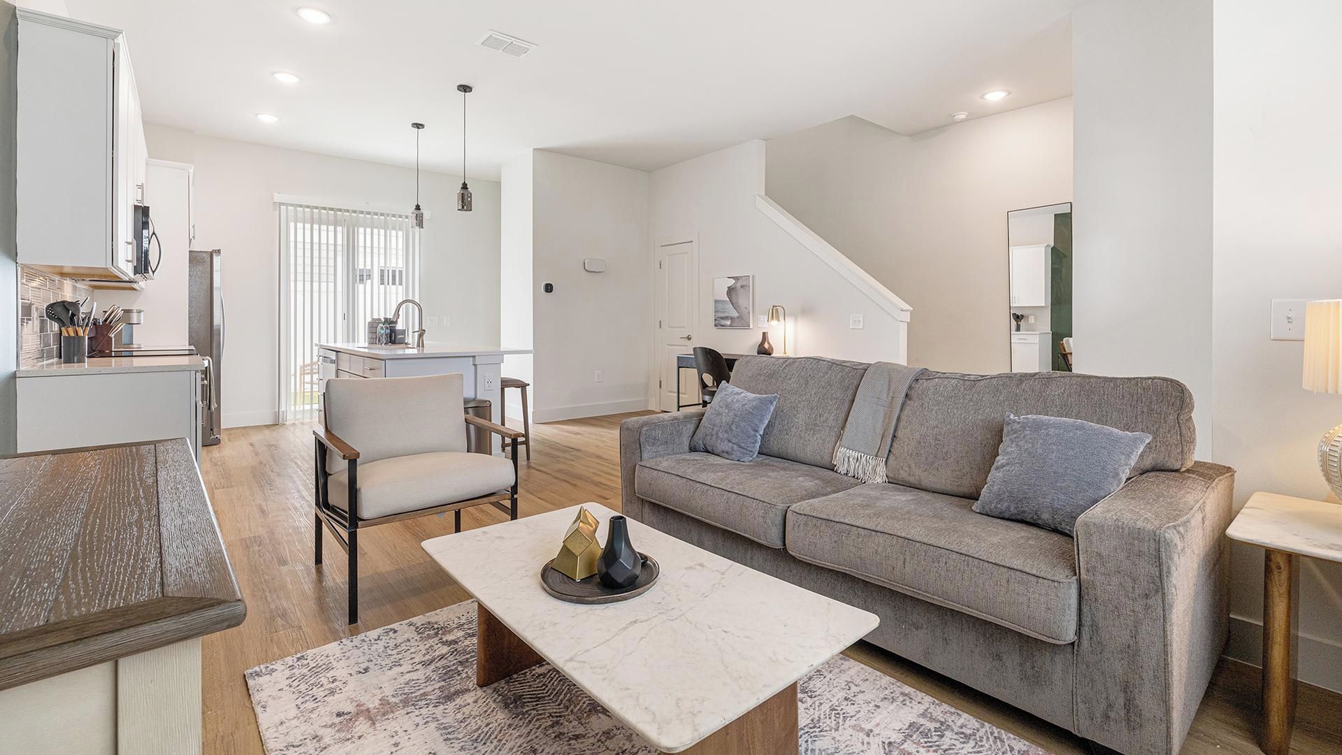 A modern living room with a sofa, coffee table, and a dining area with a kitchen in the background.