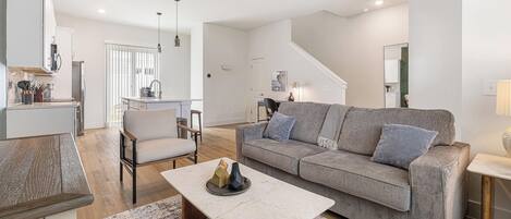 A modern living room with a sofa, coffee table, and a dining area with a kitchen in the background.