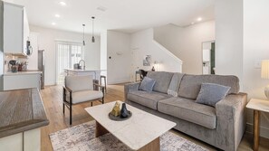 A modern living room with a sofa, coffee table, and a dining area with a kitchen in the background. - Landing | Modern 2BD, Gym (Palmetto)
