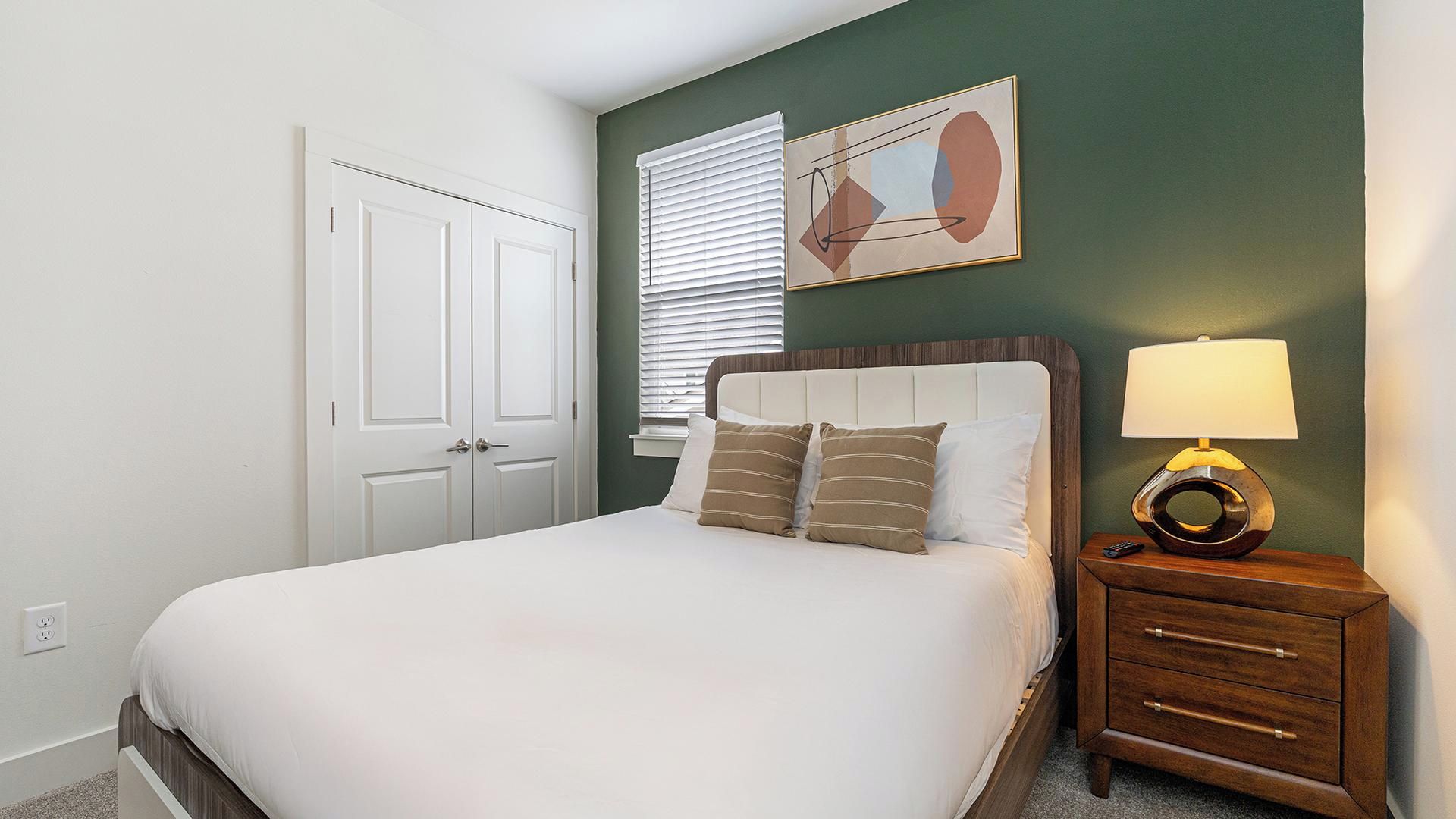 A bedroom with a bed, bedside table, lamp, and a painting on the wall.