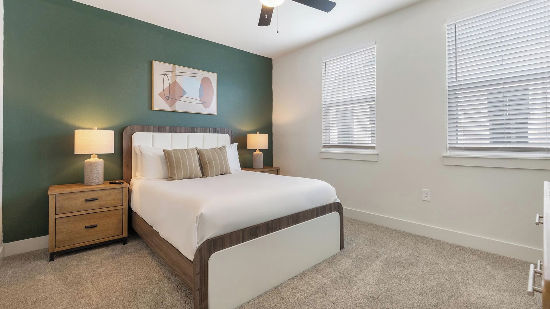 Un dormitorio con cama, mesitas de noche, ventilador de techo y una ventana con persianas.