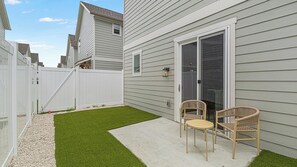 A backyard with artificial grass, a white fence, and two wicker chairs. - Landing | Modern 2BD, Gym (Palmetto)