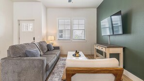 A living room with a grey sofa, a coffee table, a lamp, and a TV mounted on the wall. - Landing | Modern 2BD, Gym (Palmetto)