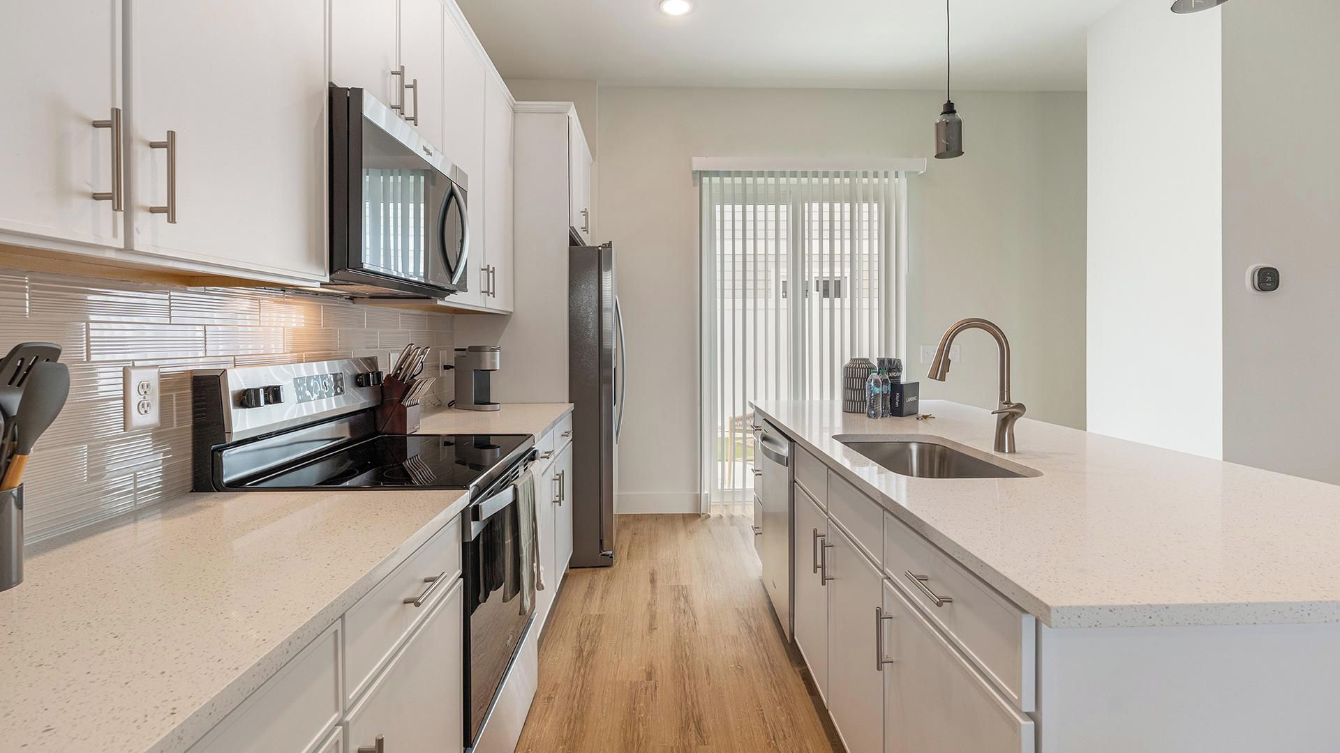 A modern kitchen with stainless steel appliances, a central island, and a view to the outside.