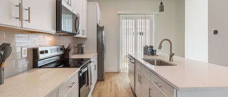 A modern kitchen with stainless steel appliances, a central island, and a view to the outside.