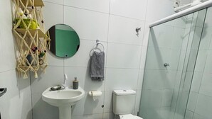 Casa de banho com cabine de chuveiro em vidro, sanita, lavatório e um ornato na parede.
