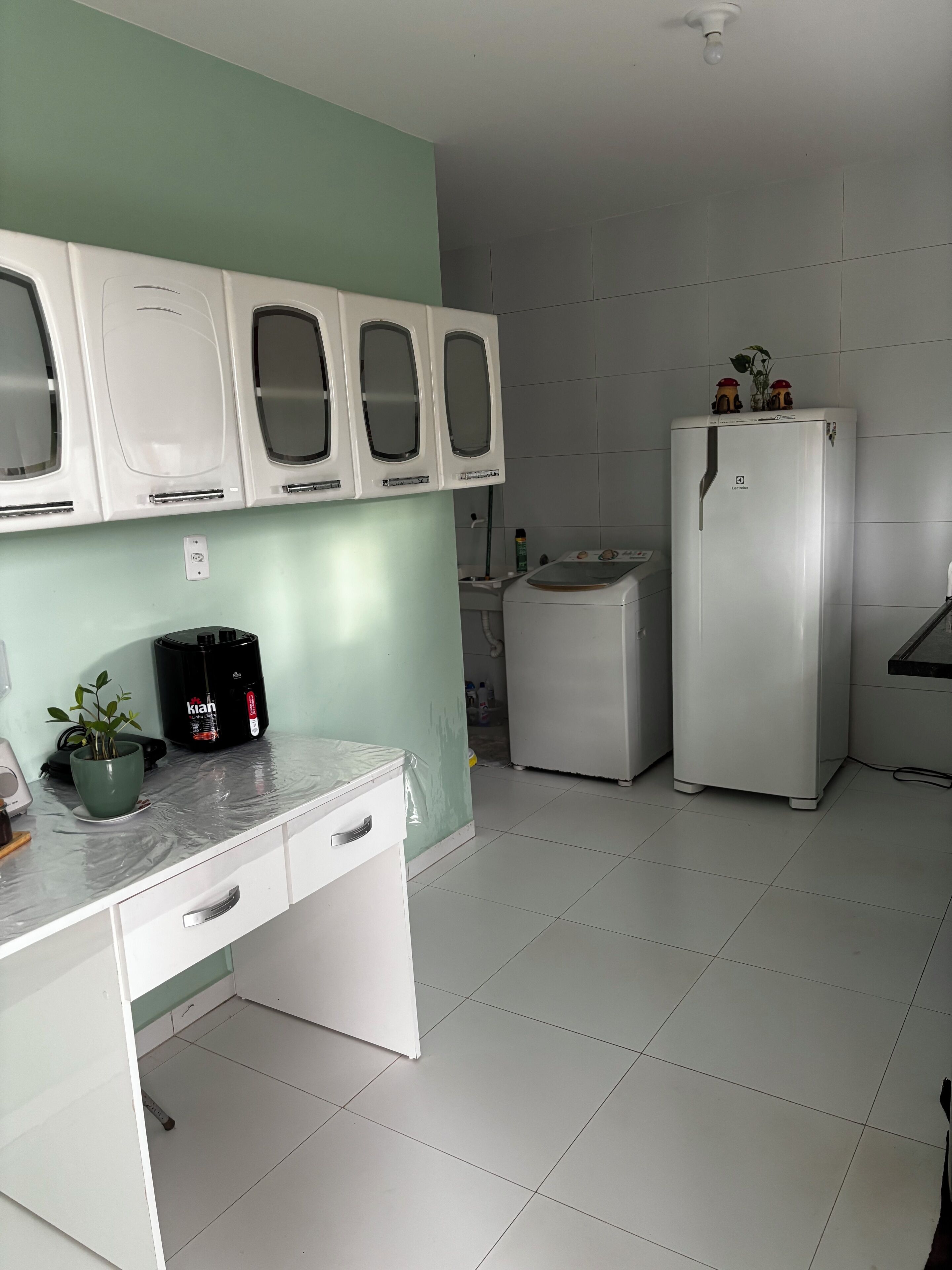 Eine Küche mit weißer Arbeitsplatte, Spüle, Kühlschrank und Schränken darüber.