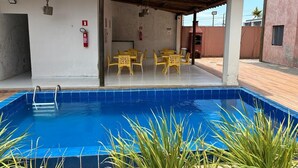 Piscina com área de estar coberta, cadeiras amarelas e um extintor de incêndio na parede.