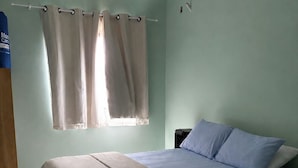 Quarto com cama, mesa de cabeceira, janela com cortinas e guarda-roupa de madeira.