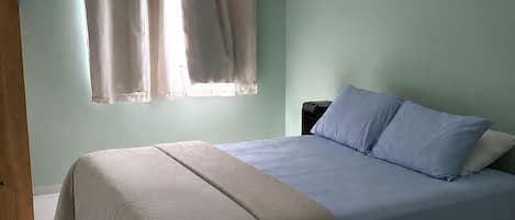 Un dormitorio con cama, mesita de noche, ventana con cortinas y armario de madera.