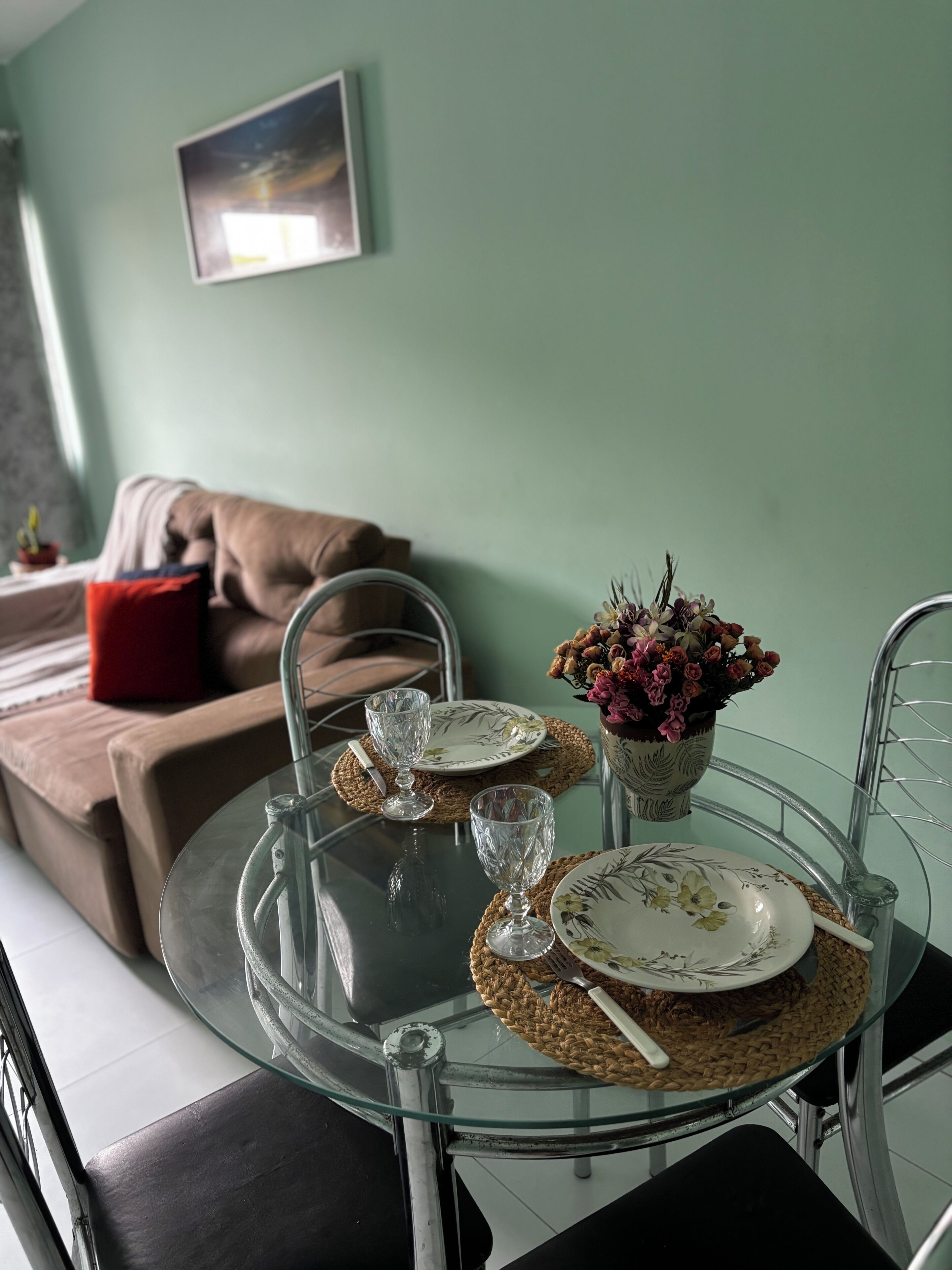 Zona pranzo con tavolo in vetro, piatti, posate e un vaso di fiori.