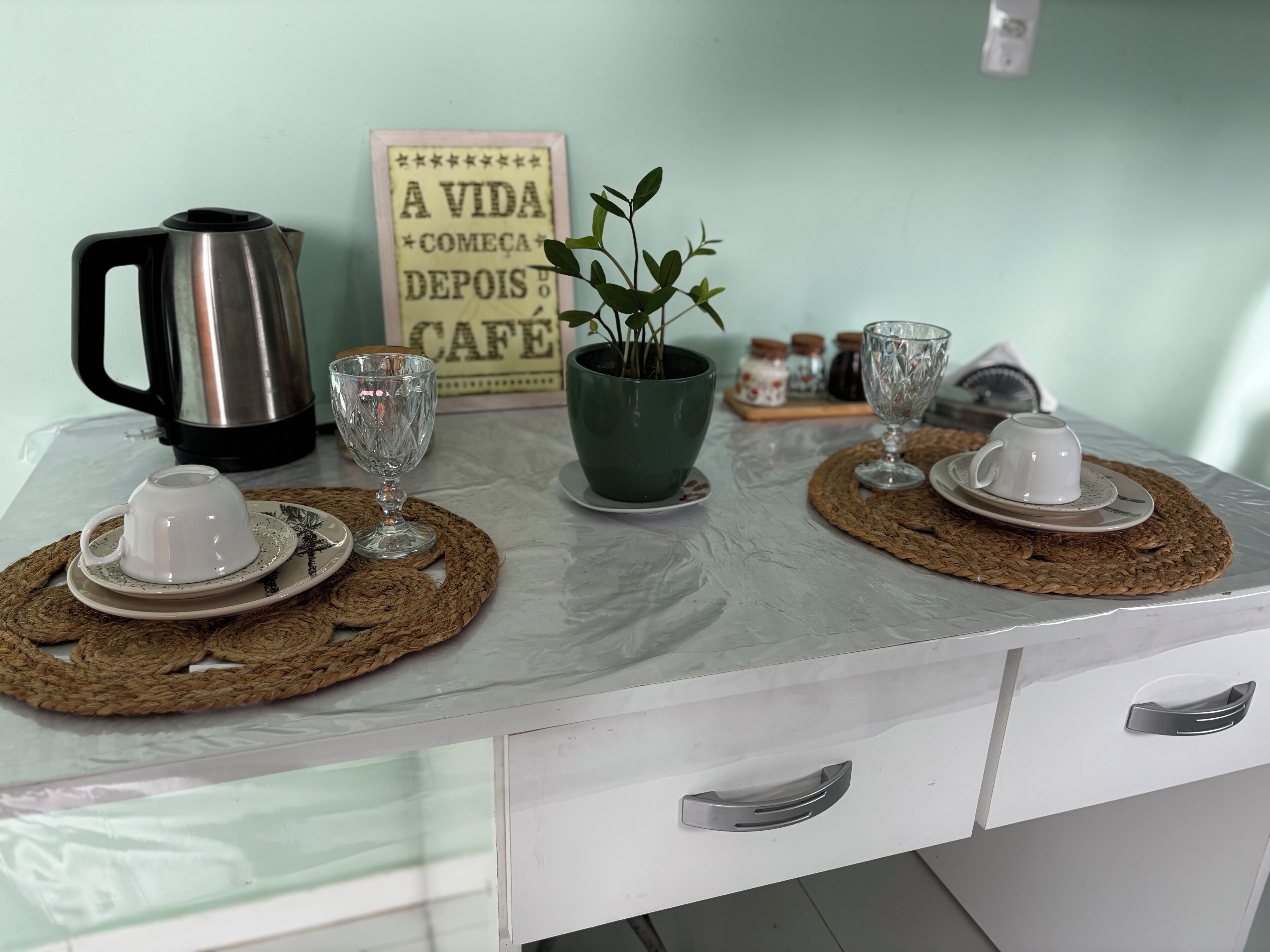 A kitchen counter with a coffee maker, two cups, a potted plant, and a sign.