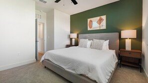 A bedroom with a bed, two bedside tables with lamps, a door, and a wall with a framed picture. - Landing | Spectacular 2BD, Gym (Palmetto)