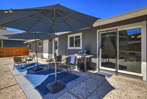 Ein Terrassenbereich im Freien mit Grill, Sitzgelegenheiten und einem großen Sonnenschirm.