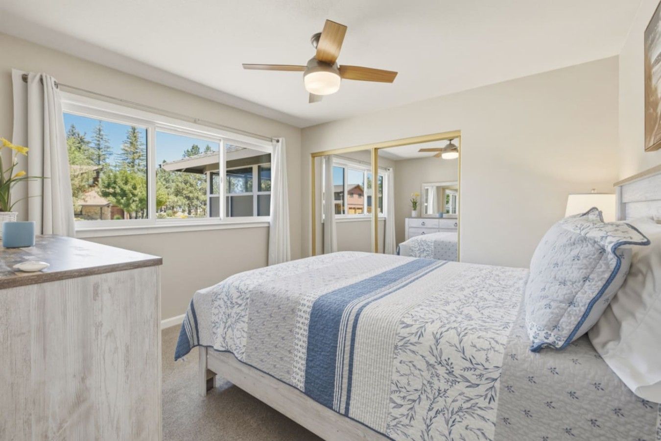 A bedroom with a bed, a desk, a ceiling fan, a window, and a mirror.