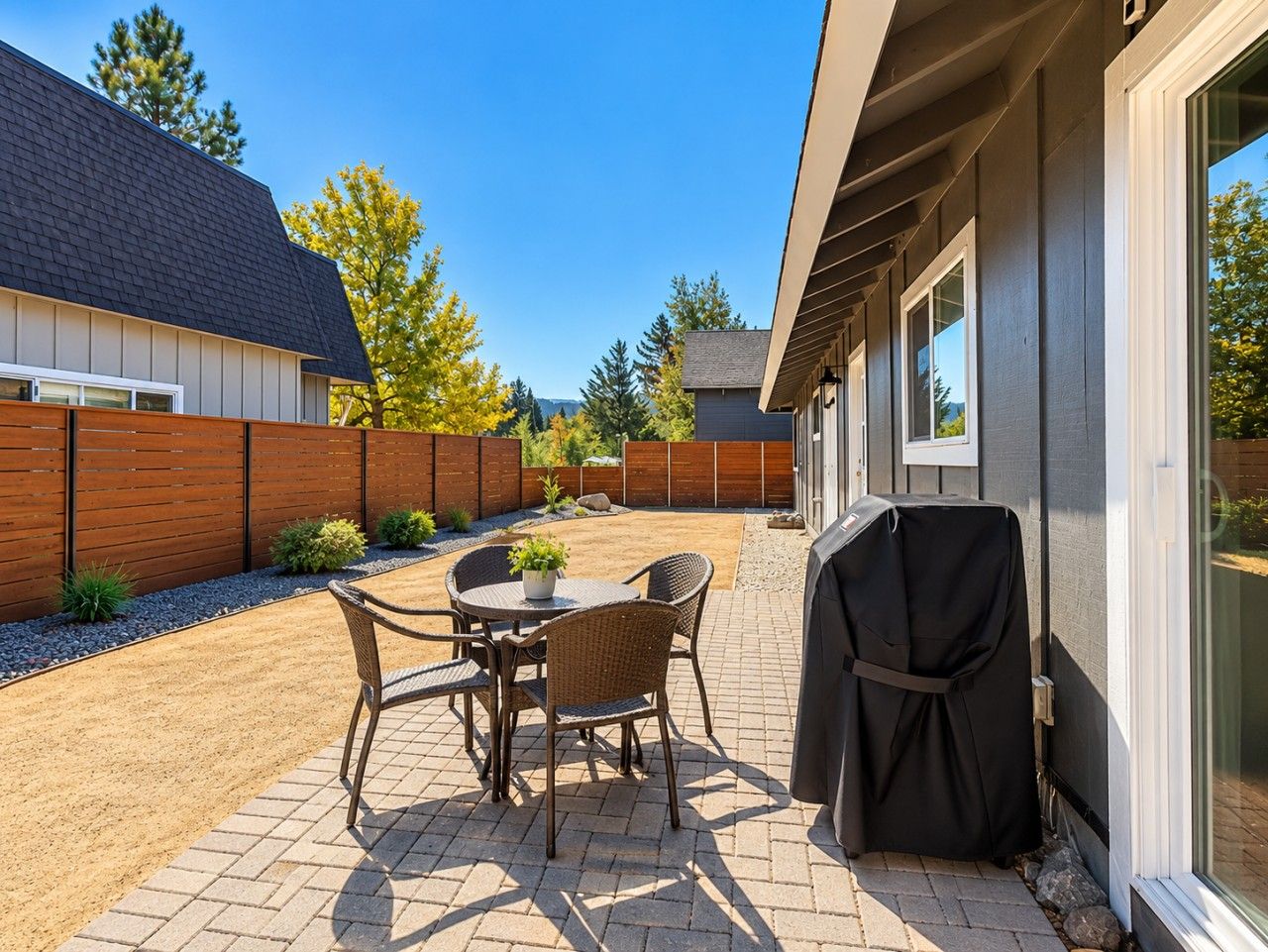 An outdoor patio with a table and chairs, a barbecue grill, and a wooden fence.