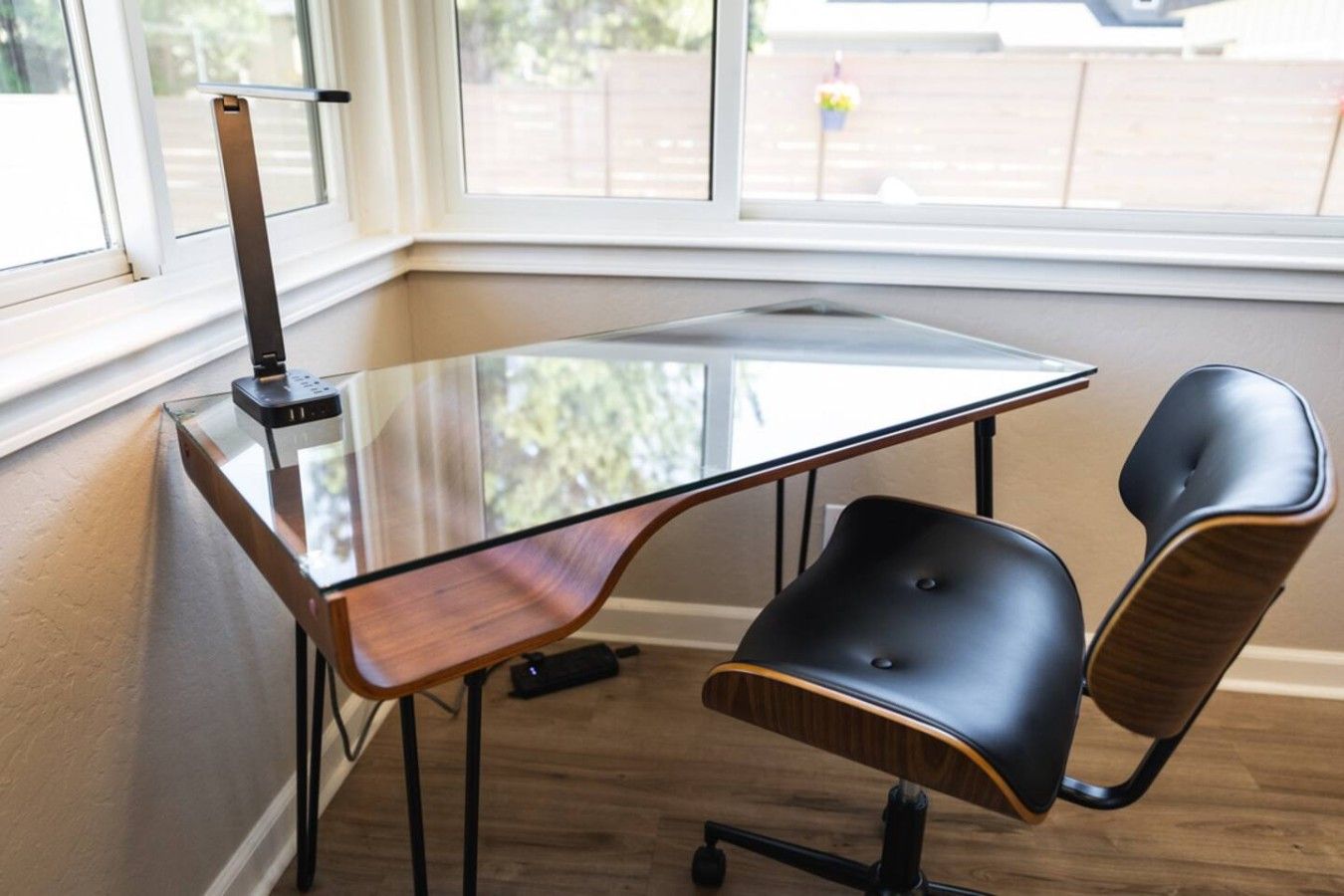 A corner workspace with a glass table, two black chairs, and a laptop.